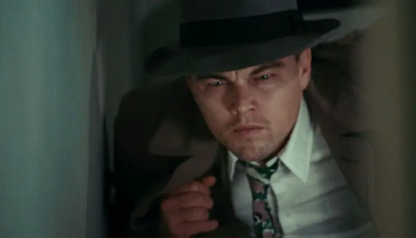 Leonardo DiCaprio, dans la distribution de Shutter Island, porte un chapeau et un trench-coat, l'air intense et méfiant.