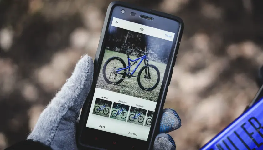 Rękawiczka trzyma smartfon z niebieskim rowerem na ekranie. Aplikacja oferuje filtry, jak w mapach rowerowych.