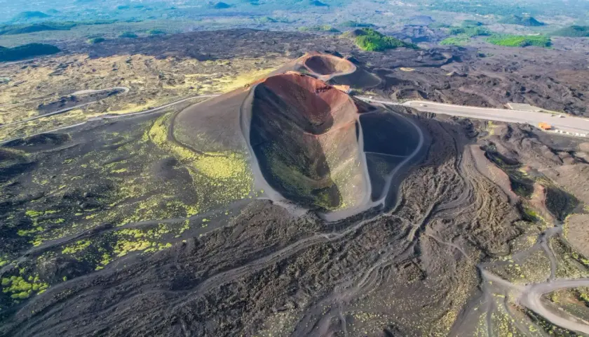 Vista aerea dei crateri spenti del vulcano Etna, con sentieri che si snodano tra la lava nera e la vegetazione gialla. Un'emozionante visita al Monte Etna.
