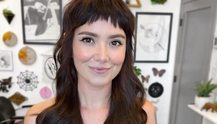 Uśmiechnięta kobieta z ciemnymi włosami i odważnymi baby bangs.