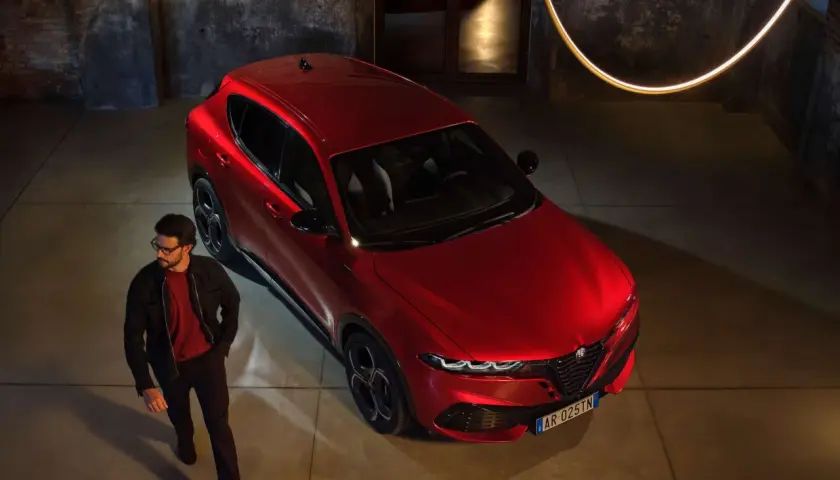 Elegancki mężczyzna w okularach obok lśniącego, czerwonego Alfa Romeo Tonale. Sprawdź aktualną alfa romeo tonale cena i odkryj jego styl.