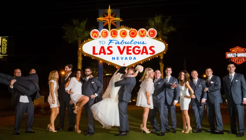Ślub w Las Vegas jest ważny w Polsce? Para młoda całuje się pod neonem "Welcome to Fabulous Las Vegas", otoczona przez świadków.