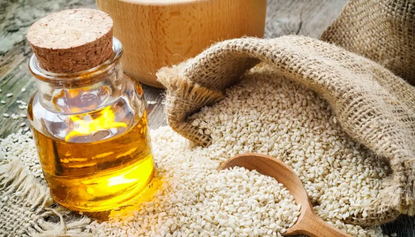 Olio di sesamo dorato in bottiglia, semi di sesamo in un sacco di juta e un cucchiaio di legno. Scopri le incredibili olio di sesamo proprietà.