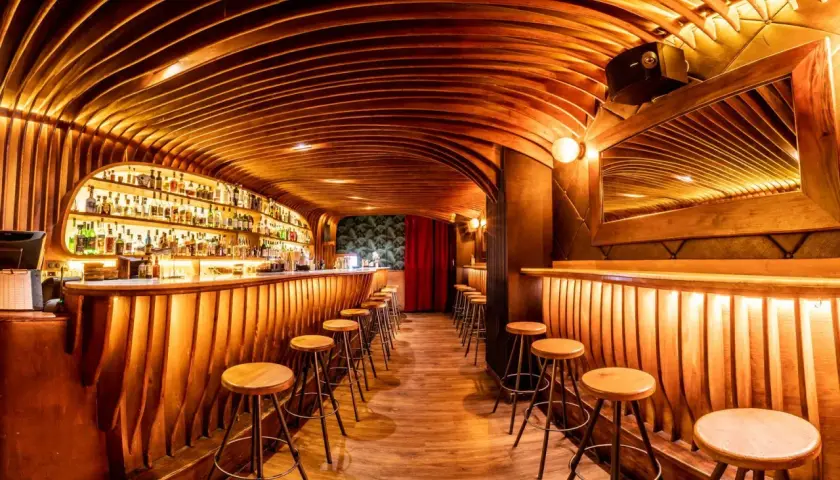 Bar de madera con estantes llenos de botellas, taburetes y un techo curvo. ¡Cosas curiosas que ver en Barcelona!
