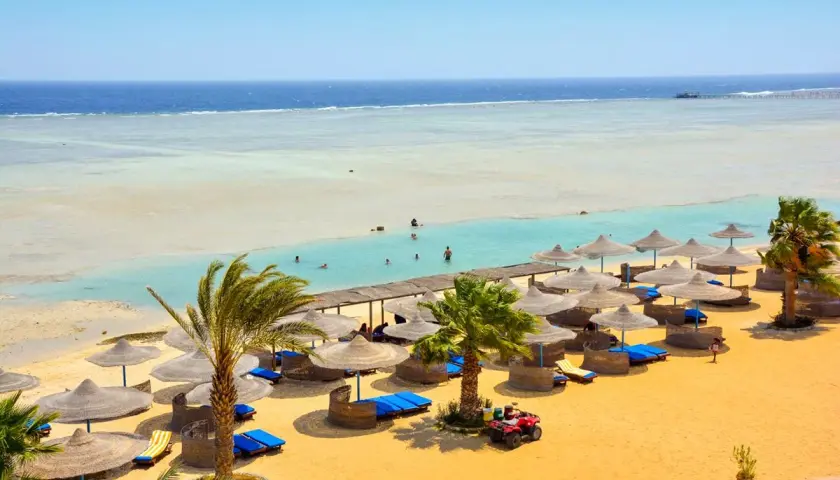 Piękna plaża z palmami i leżakami, idealna na wakacje. Wiele osób pływa w turkusowej wodzie. Blue Reef Resort opinie potwierdzają rajski wypoczynek.