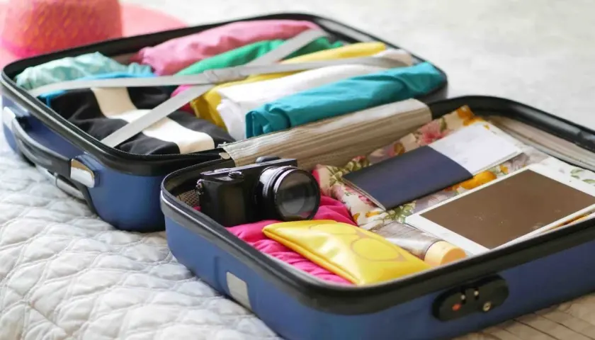 Valise ouverte prête pour un EVJF : vêtements colorés, appareil photo, passeport, tablette. Une liste valise EVJF drôle à compléter !