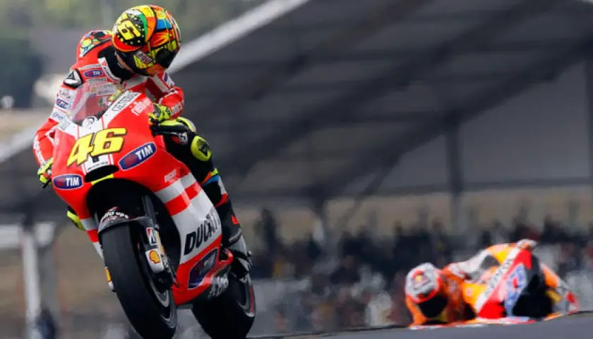 Valentino Rossi en su Ducati, número 46, inclinado en una curva. Otro piloto yace en el suelo.