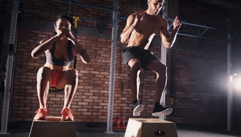 Para i mężczyzna wykonują trening crossfit, skacząc na skrzynie.