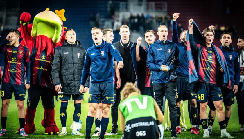 Piłkarze ze Szczecina świętują zwycięstwo. Na murawie widać też maskotkę klubu i fotoreportera.