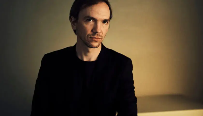 Portret Jana Komasy, reżysera znanych filmów. Jego spojrzenie sugeruje głębię i skupienie, jak w jego kinowych dziełach.