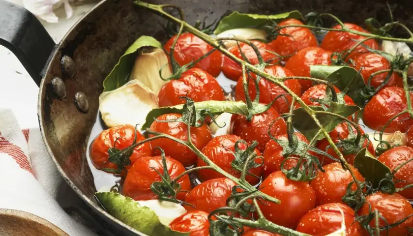 Saftige cherry tomaten mit Knoblauch und Lorbeerblättern in einer Pfanne, bereit zum Garen.