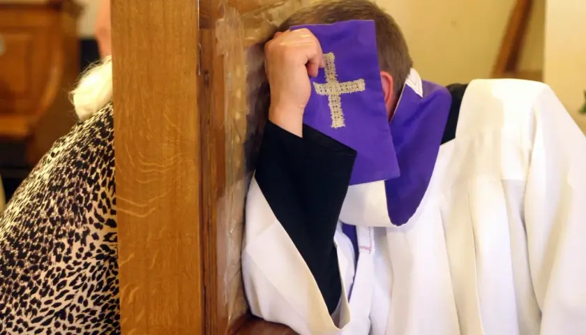 Spowiedź w konfesjonale. Czy nie pójście do kościoła z powodu choroby to grzech? Kapłan w białej albie i fioletowej stuły z krzyżem.