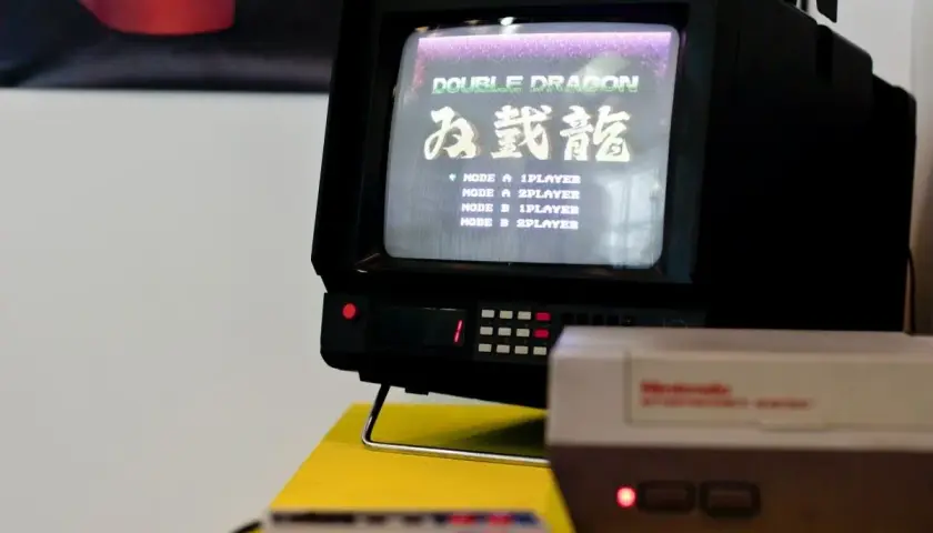 Stary telewizor Thomson z grą Double Dragon. Na ekranie widoczna lista trybów gry, np. "MODE A 1PLAYER". Obok konsola Pegasus.