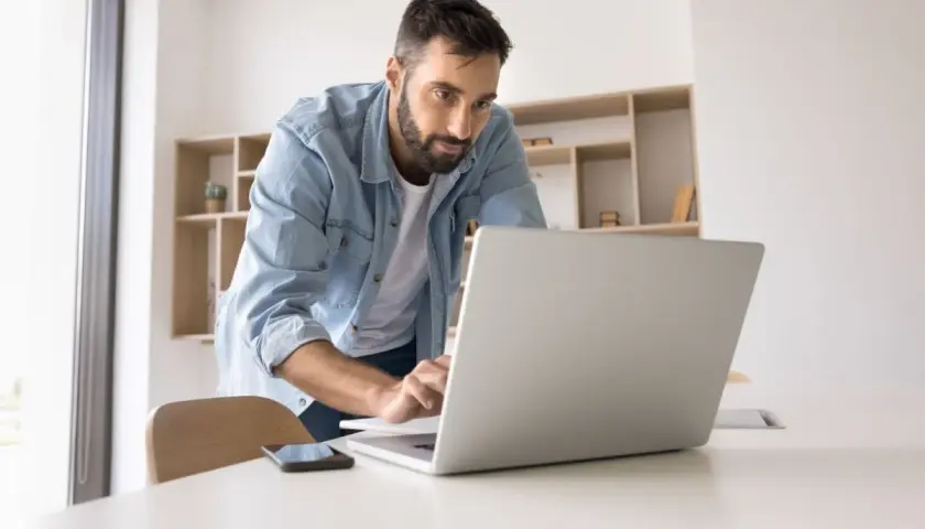 Mężczyzna w dżinsowej koszuli pracuje przy laptopie, analizując swój stosunek pracy.