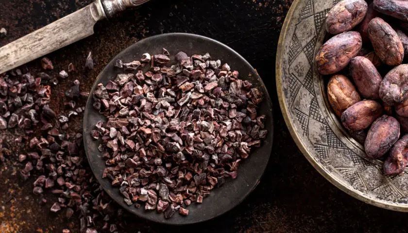 Un coltello d'argento accanto a una ciotola di **semi di cacao** tritati e un piatto decorato con semi di cacao interi.