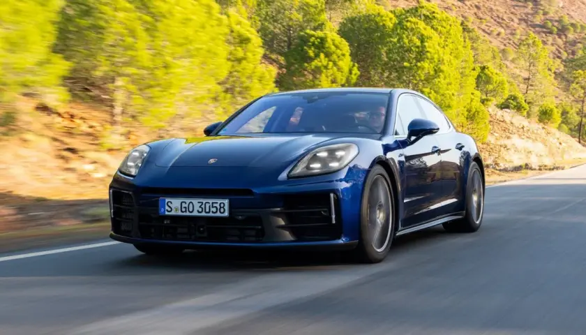 Niebieski Porsche Panamera 2024 pędzi po krętej drodze wśród zielonych wzgórz.