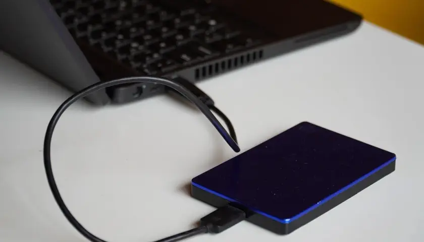 Un disque dur externe bleu est connecté à un ordinateur portable. Un guide pour comment choisir son disque dur externe.