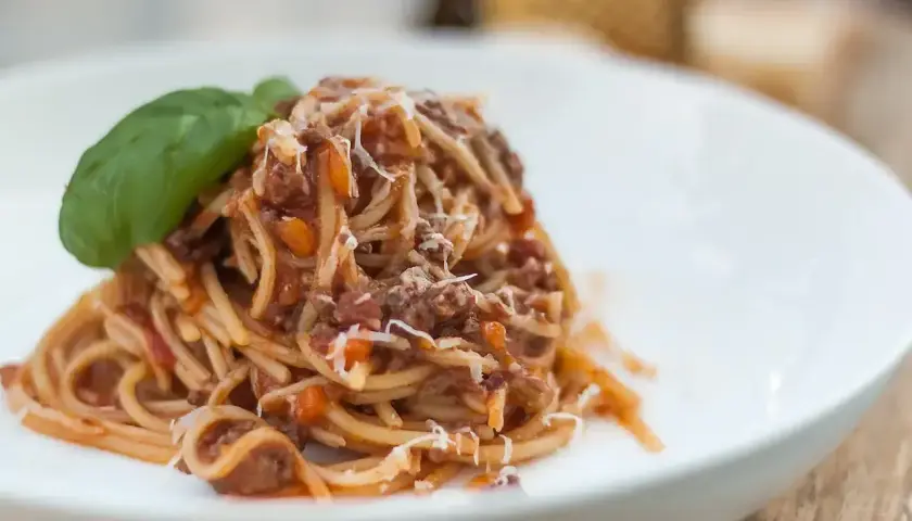 Pyszne spaghetti z sosem ragu, posypane parmezanem i udekorowane listkiem bazylii. Idealny przepis na obiad.
