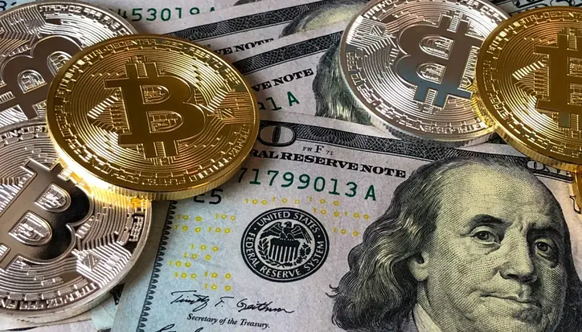Złote i srebrne monety z symbolem Bitcoina leżą na banknotach dolarowych. Czy to przyszłość płatności w kantorze Santander Bank?