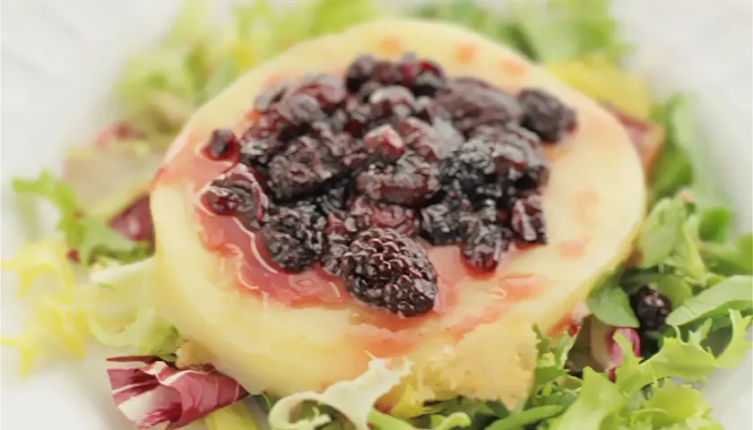 Provolone a la plancha cubierto con moras y salsa, servido sobre una cama de lechugas mixtas.