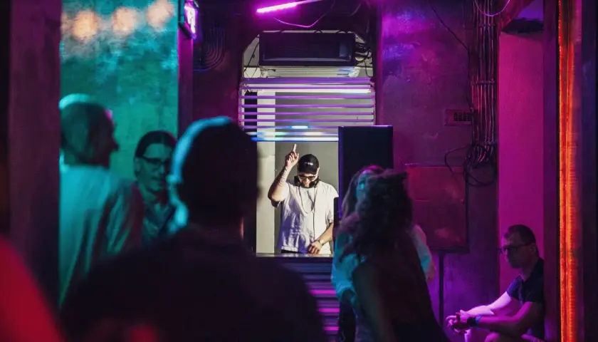 DJ w klubie, podniesiony palec, neonowe światła, różowy sober tekst.