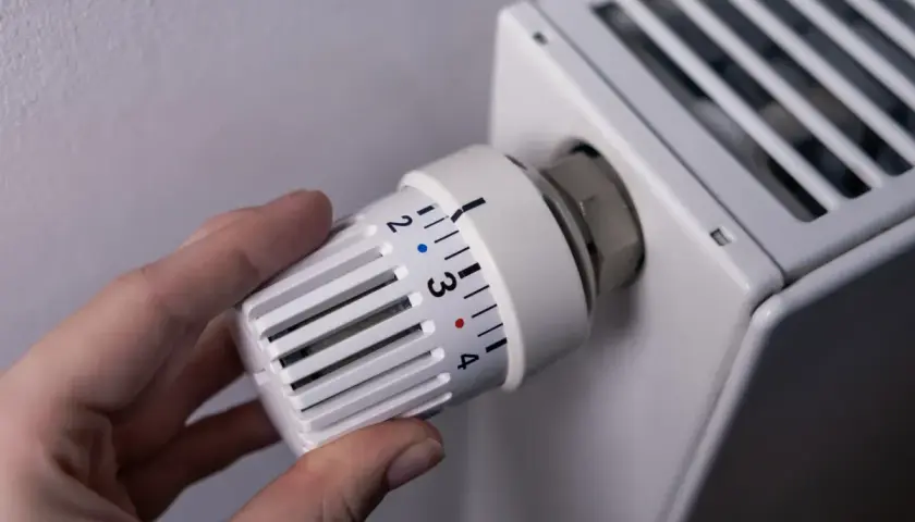 Dłoń reguluje termostat grzejnika, kontrolując ogrzewanie domu na gaz. Ustawienie temperatury na 3.