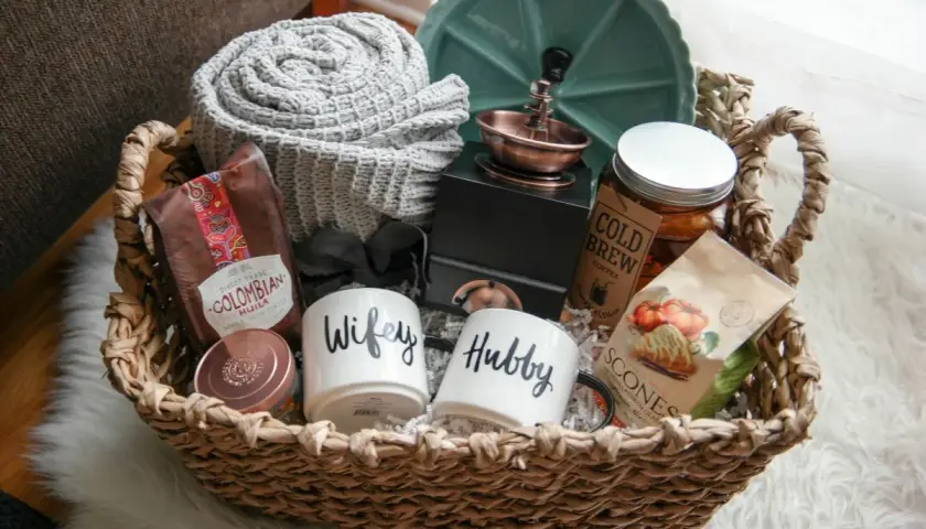 Cesta de mimbre con un kit para recién casados: tazas "Wifey" y "Hubby", café colombiano, scones, manta y más.
