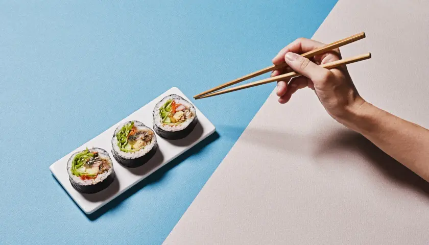Dłoń z pałeczkami do sushi pokazuje, jak trzymać pałeczki do sushi, by złapać pyszne rolki.