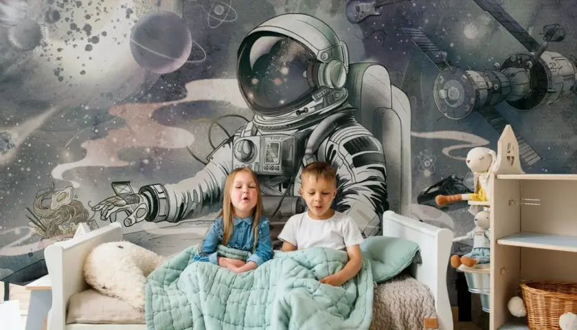 Dzieci siedzą pod kołdrą na łóżku, a za nimi wspaniała tapeta kosmos dla dzieci z astronautą i planetami.