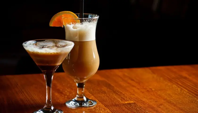 Dwa drinki z likierem kawowym i mlekiem: jeden w kieliszku martini, drugi w wysokiej szklance z pomarańczą.