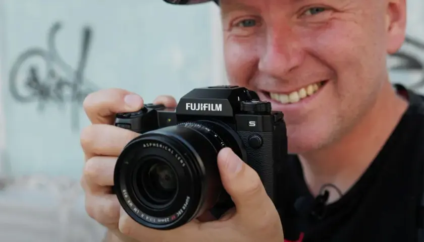 Uśmiechnięty mężczyzna trzyma aparat Fujifilm XH2S z obiektywem.