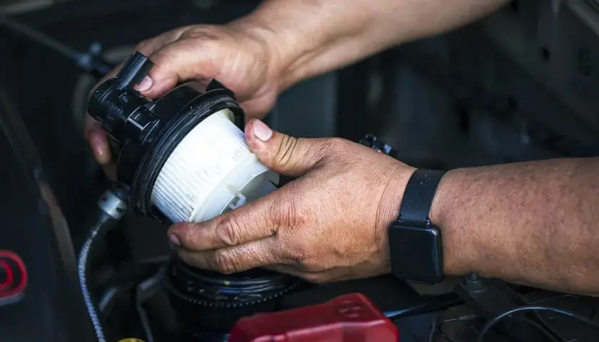 Ręce mechanika wymieniające filtr paliwa w samochodzie.