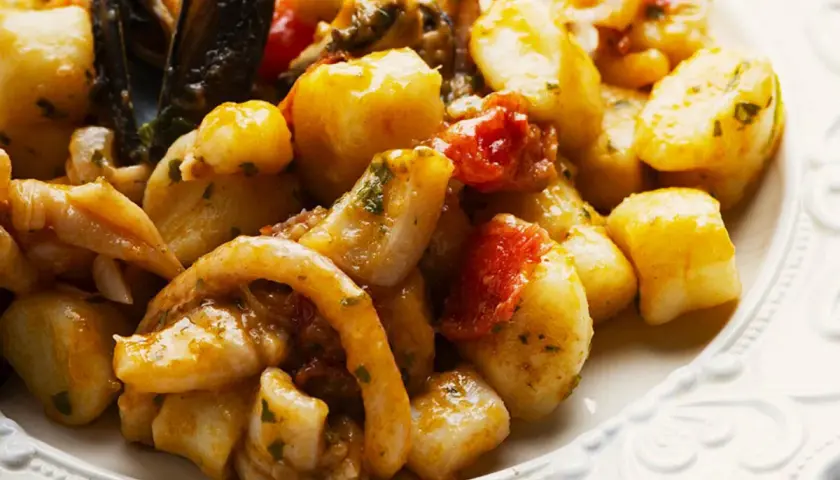 Gnocchi allo scoglio con cozze, calamari e pomodorini, un piatto ricco di sapori marini.