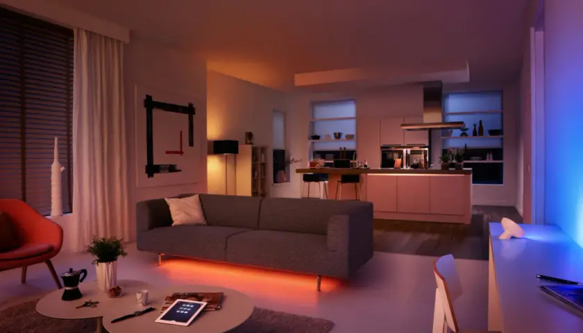 Sofá moderno con iluminación led ambiental. Cocina integrada, arte abstracto y silla naranja. Las led caracteristicas crean una atmósfera acogedora.