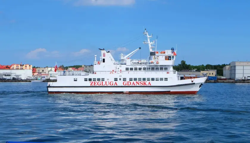 Biały tramwaj wodny "Żegluga Gdańska" płynie po morzu, w tle widać zabudowania Gdyni i Helu.