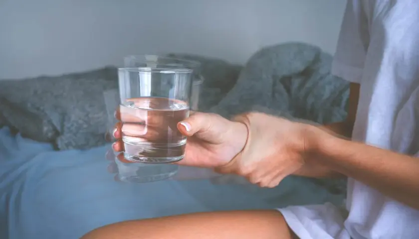 Drżąca ręka trzymająca szklankę wody, symbolizująca objawy padaczki alkoholowej.