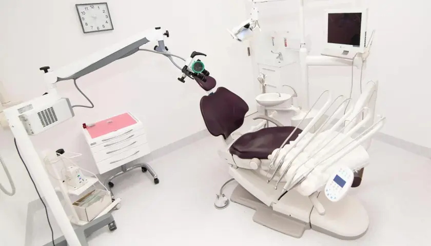 Nowoczesny gabinet stomatologiczny z fotelem, mikroskopem i sprzętem.
