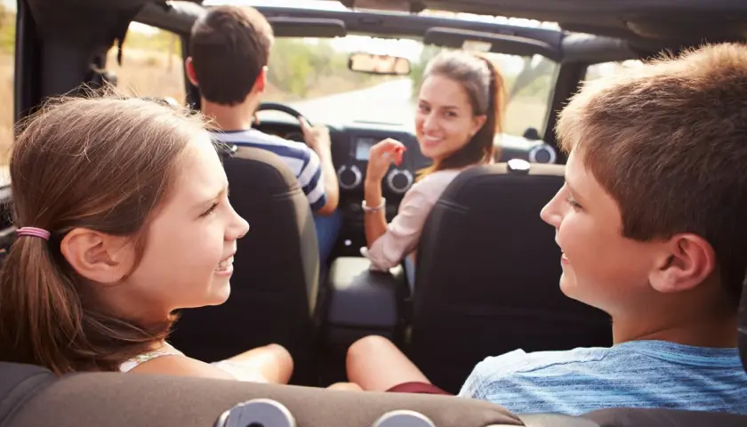 Famiglia in auto, divertiti con giochi da fare in macchina a voce. I bambini sorridono, la madre guarda indietro.