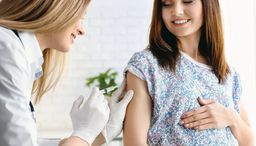 Ärztin verabreicht schwangerer Frau Impfung. Boostrix Polio schützt Mutter und Kind.
