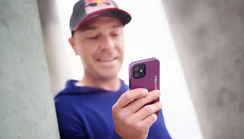 Mężczyzna w czapce Red Bull trzyma telefon z wzorzystym etui. Wzory na telefonie są czerwono-niebieskie.