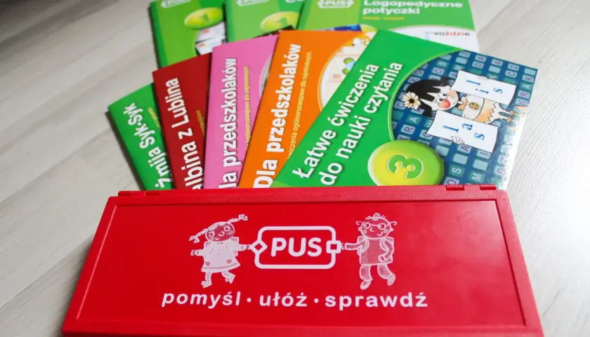 Czerwone pudełko z zabawkami edukacyjnymi PUS i kolorowe książeczki.