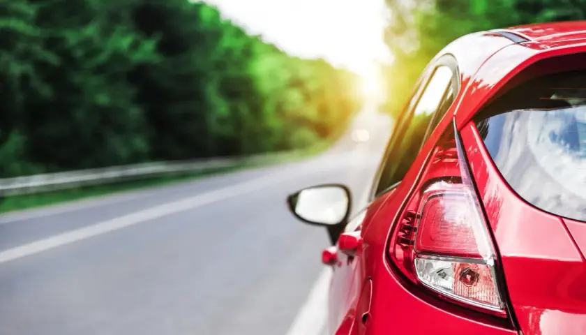 Auto rossa su strada panoramica, con sole che filtra tra gli alberi. Potrebbe indicare una **perdita potenza motore benzina** durante un viaggio.