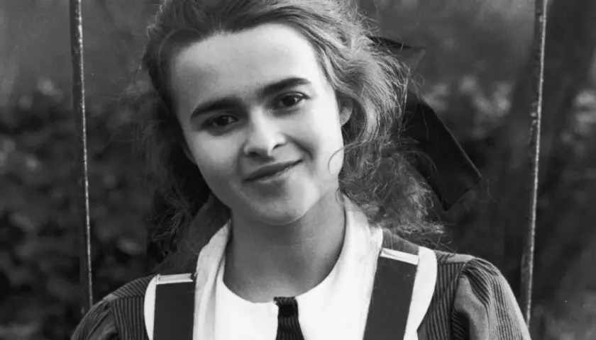 Młoda Helena Bonham Carter z burzą loków i figlarnym uśmiechem, w stroju przypominającym szkolny mundurek.
