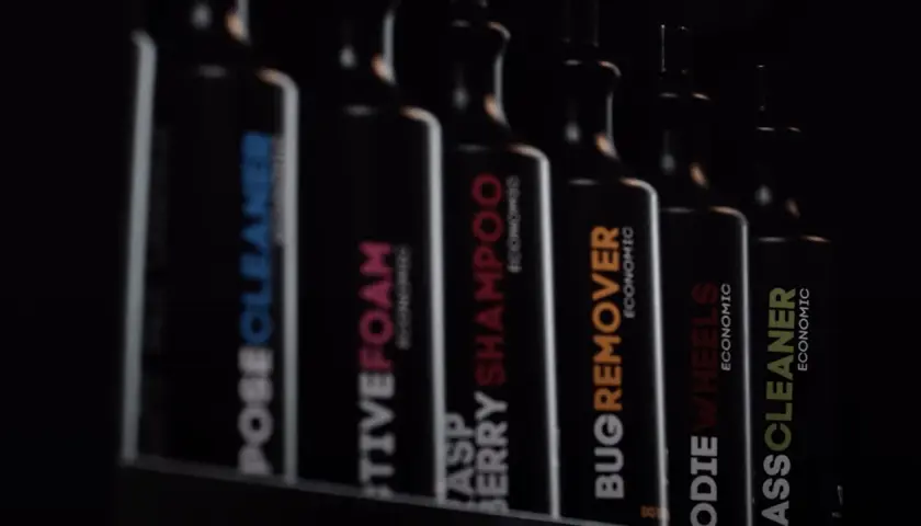 Rząd czarnych butelek z etykietami: "POSECLEANER", "CTIVEFOAM", "RASPBERRY SHAMPOO", "BUGREMOVER", "ODIE WHEELS", "ASSCLEANER". To są kosmetyki do samochodu.