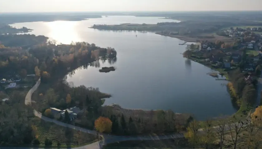 Jesioro Kałębie w jesiennej odsłonie, z widokiem na spokojną taflę wody, otoczoną drzewami w barwach złota i czerwieni.
