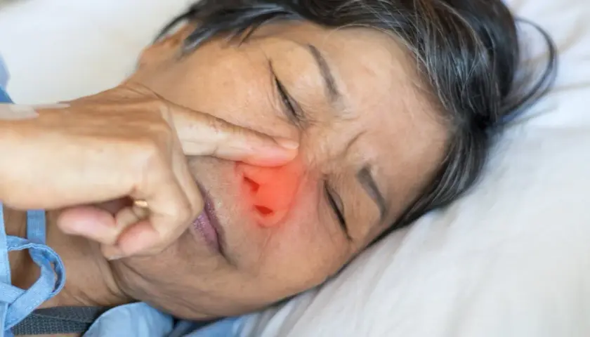Una persona mayor con un dedo en la nariz, con una zona roja que indica dolor o irritación. ¿Qué pasa si te comes los mocos?