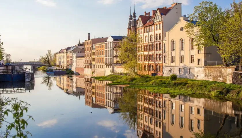 Nad rzeką w Opolu, zabytkowe kamienice odbijają się w spokojnej wodzie. To piękne opole atrakcje, które warto zobaczyć.