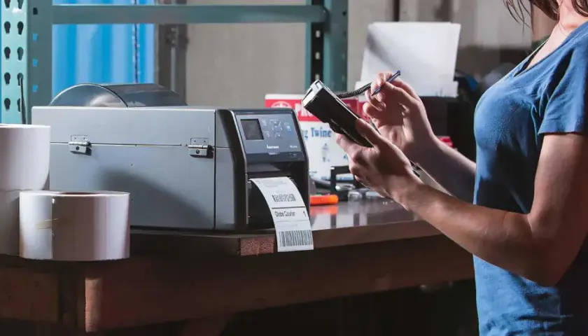 Frau bedient Drucker für Etiketten und Handscanner. Dies ermöglicht effizientes belegloses kommissionieren im Lager.