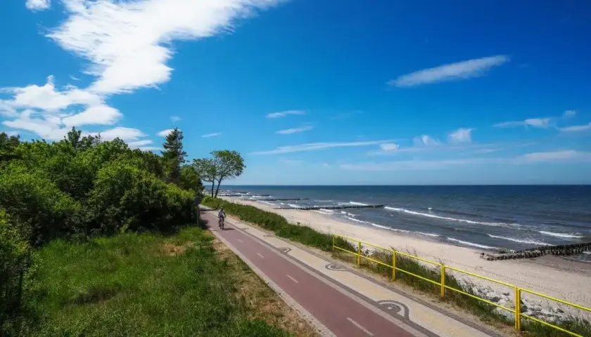 Rowerzysta przemierza ścieżkę nad polskim morzem. Idealne miejsce na wakacje, z zielenią i błękitem nieba.