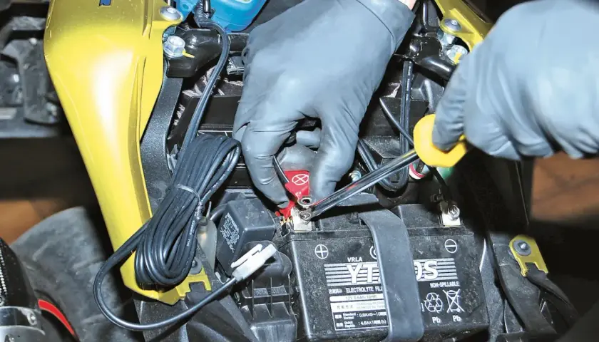 Mani guantate usano una chiave per staccare la batteria moto.